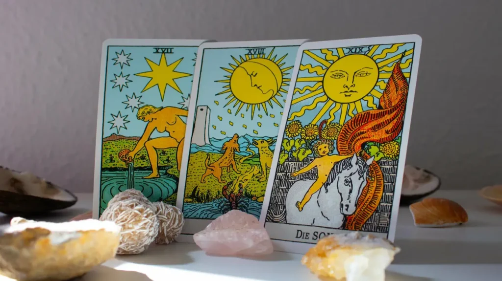 Una imagen de tarot mística y luminosa para el blog "Regresar con mi ex". Muestra tres cartas clave alineadas: La Estrella, La Luna y El Sol (en alemán, "DIE SONN"). Estas cartas simbolizan la esperanza, la sanación emocional, el reencuentro y el triunfo del amor verdadero tras una separación. Las cartas están rodeadas de cristales curativos como cuarzo rosa y citrino, y conchas marinas, enfatizando la energía de renovación y felicidad para una pareja que desea volver a estar junta.