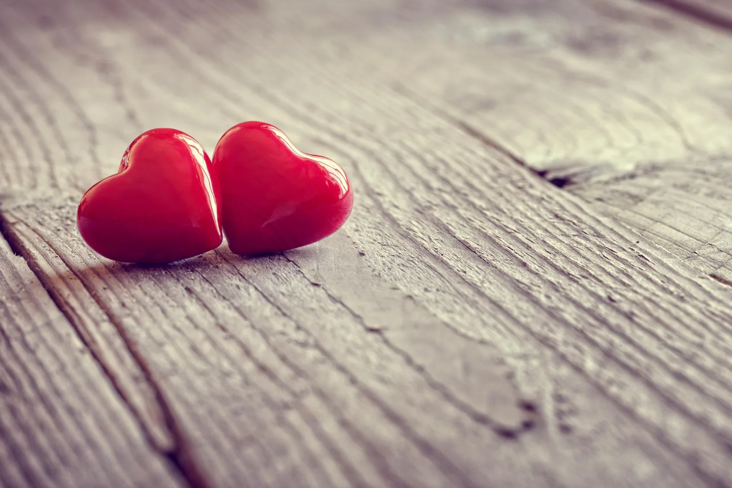 Dos corazones rojos brillantes y unidos sobre una mesa de madera rústica, utilizados para ilustrar conceptos de tarot amoroso y rituales para recuperar a un ex. La imagen simboliza la unión de la pareja, la pasión renovada y la estabilidad emocional necesaria para una reconciliación exitosa. El enfoque suave y la calidez de la madera evocan la esperanza y la sanación de los lazos sentimentales tras una ruptura.